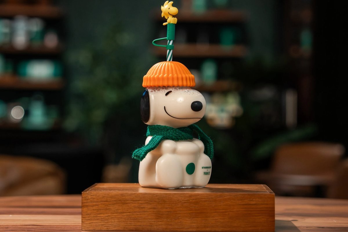 Starbucks Snoopy cup with an orange beanie, green scarf and Woodstock straw topper